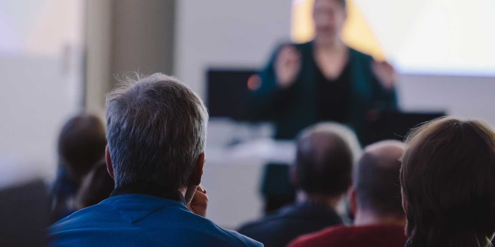 Yleisöä istumassa ja katsomassa edessä seisovaa hahmoa.